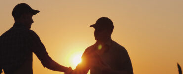 Dois produtores rurais apertando as mãos em frente ao pôr do sol.