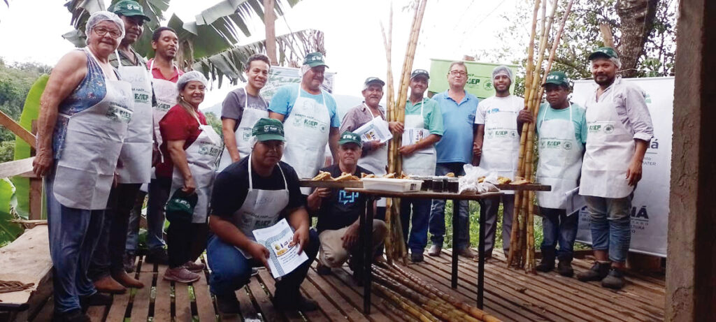 Turma do curso de produção de cachaça e de derivados de cana-de-açúcar, realizado pelo SENAR-PR em Adrianópolis, expondo os produtos fabricados em uma mesa.