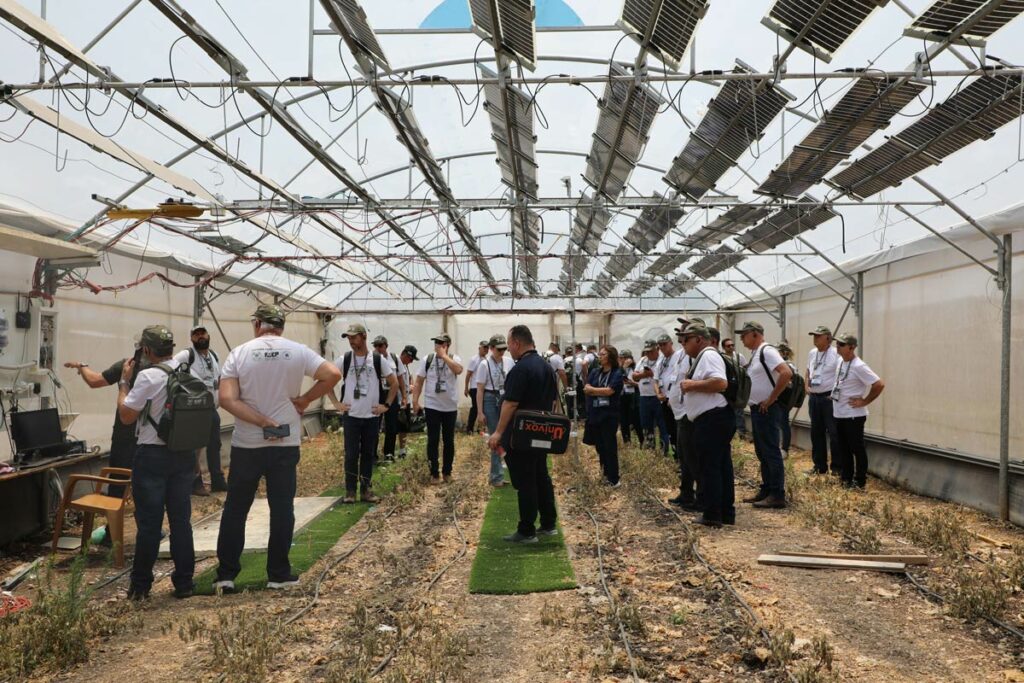 Grupo de pessoas visitando uma estufa de um centro de pesquisa em Israel, onde há painéis de energia solar instalados no teto e sistema de irrigação no chão.