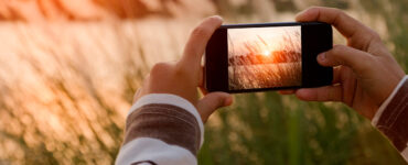 Pessoa tirando foto de uma paisagem com pôr do sol com um celular na horizontal.