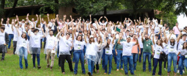 Participantes do Agrohackathon com os braços levantados em uma foto tirada ao ar livre