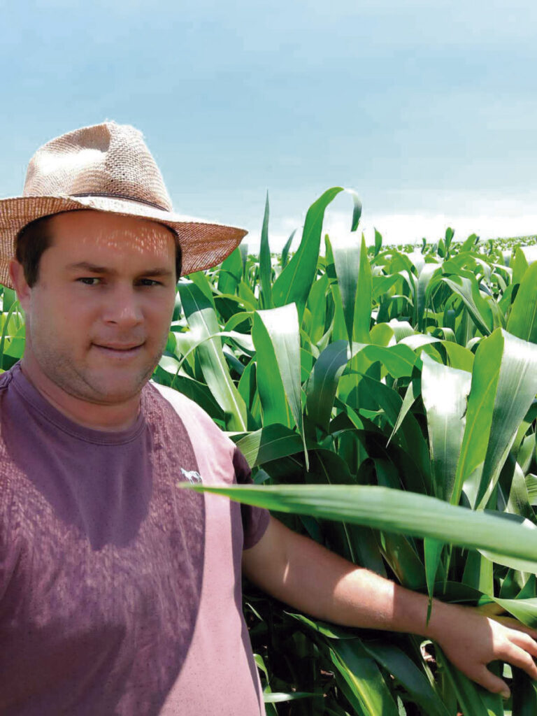 Produtor rural com lavoura de milho ao fundo e céu azul