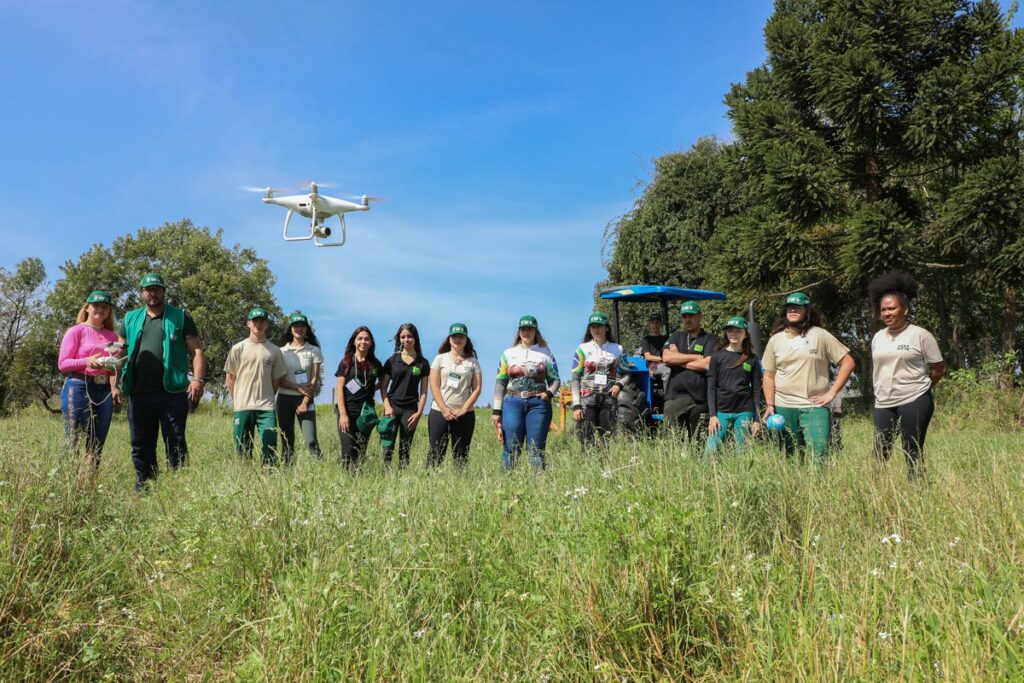 Estudantes em campo aberto com pastagem e floresta operando drones graças a projeto em parceria com o SENAR-PR
