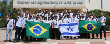 Viagem Técnica a Israel 3º grupo. Pessoas em frente ao centro de pesquisa de áreas áridas com as bandeiras do Brasil e Israel.
