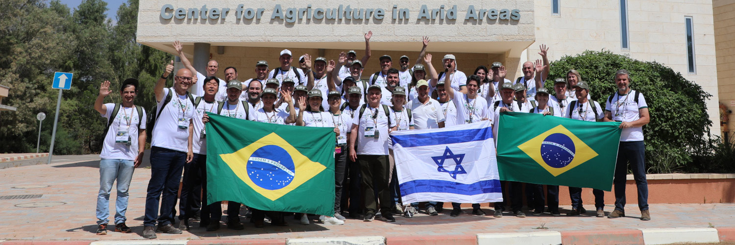 Viagem Técnica a Israel 3º grupo. Pessoas em frente ao centro de pesquisa de áreas áridas com as bandeiras do Brasil e Israel.
