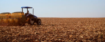 Máquina em paisagem rural trabalhando no plantio de uma área de soja com o céu azul