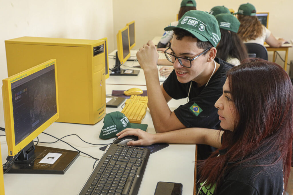 Alunos de colégio agrícola no Paraná com boné do SENAR-PR em frente a computador