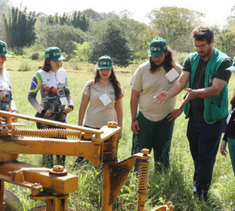 Instrutor e alunos de colégio agrícola em ação no campo, mexendo em uma máquina agrícola