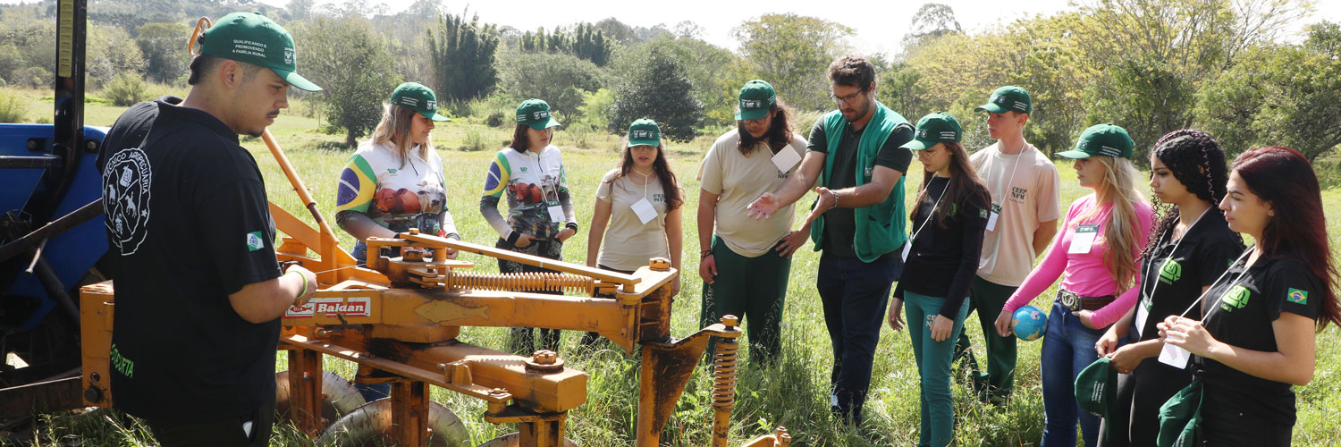 Instrutor e alunos de colégio agrícola em ação no campo, mexendo em uma máquina agrícola